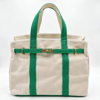 A canvas tote bag in natural beige with prominent green straps and trim, featuring a gold-tone turn-lock closure on a horizontal strap across the front.