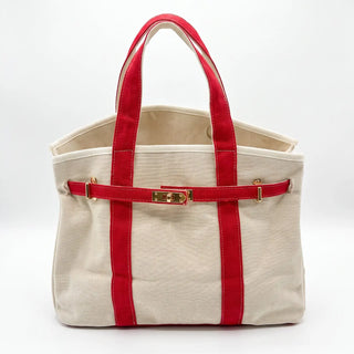 A canvas tote bag in off-white with vibrant red handles and side straps, featuring a gold-tone metal clasp on the front strap, set against a plain white studio background.