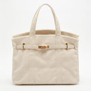 A structured canvas tote bag in a light cream or off-white color, featuring a horizontal strap across the front with gold-tone hardware and dual top handles, set against a plain white background.