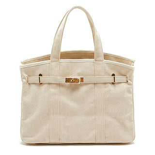 A structured canvas tote bag in a light cream or beige color, featuring a horizontal strap across the front with gold-tone metal hardware and two top handles, set against a plain white background.