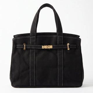 A black nylon tote bag with white contrast stitching, a front horizontal strap with gold-tone hardware, and dual top handles, shown against a plain white background.