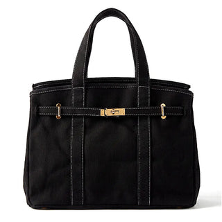 A black canvas tote bag with white contrast stitching, featuring a horizontal strap across the front with gold-tone hardware and dual top handles, set against a plain white background.
