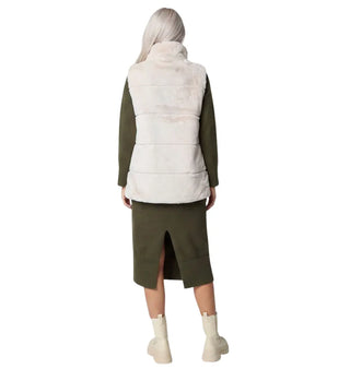 A model shown from the back wearing a cream-colored puffer vest over an olive green long-sleeve top and matching olive green skirt, paired with off-white ankle boots, on a solid white background.